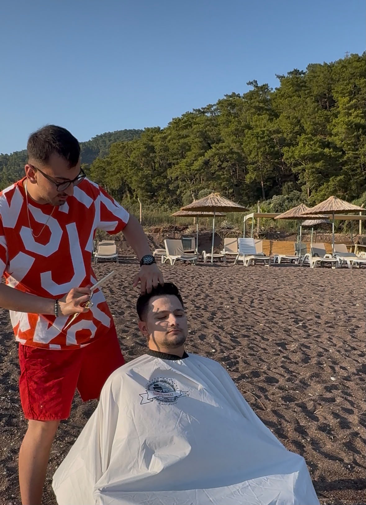 Arda Uymaz, plajda makasla saç kesimi yapıyor